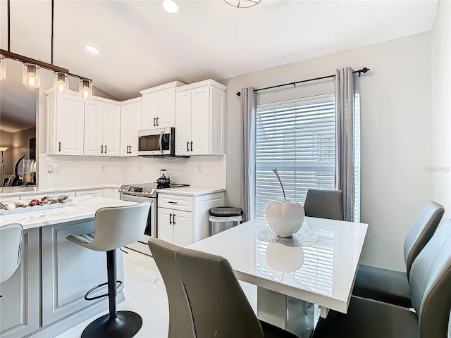 kitchen with appliances with stainless steel finishes, decorative light fixtures, vaulted ceiling, white cabinetry, and recessed lighting