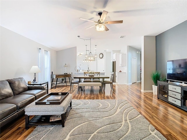 living area featuring ceiling fan with notable chandelier, visible vents, baseboards, and wood finished floors