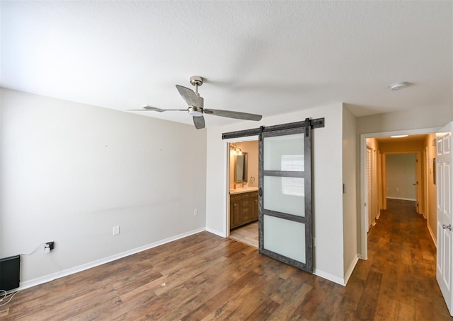 9730 Lake Chase Island Way Unit 9730, Tampa, FL 33626 - unfurnished bedroom featuring a barn door, dark wood finished floors, ensuite bathroom, and ceiling fan