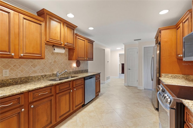 kitchen with stainless steel appliances, a sink, light stone countertops, tasteful backsplash, and brown cabinetry