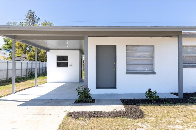 entrance to property featuring stucco siding, an attached carport, concrete driveway, and fence