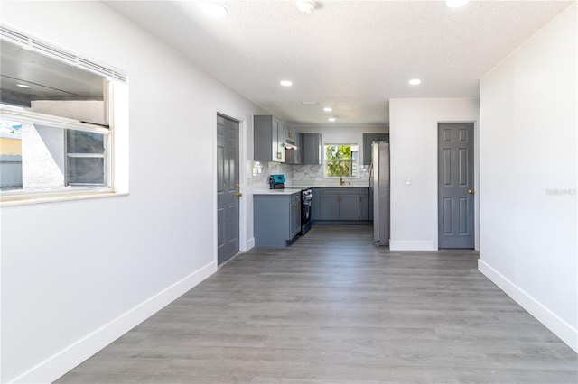 kitchen with light wood-type flooring, backsplash, stainless steel appliances, light countertops, and baseboards