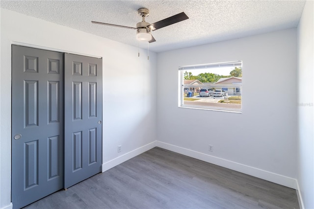 unfurnished bedroom featuring baseboards, wood finished floors, a closet, a textured ceiling, and a ceiling fan