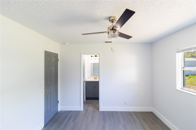 unfurnished bedroom featuring ceiling fan, a textured ceiling, baseboards, and wood finished floors