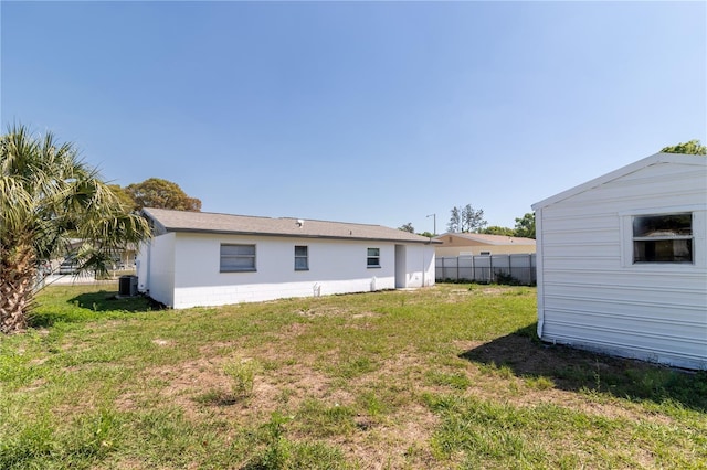 back of house featuring a lawn, an outdoor structure, and fence