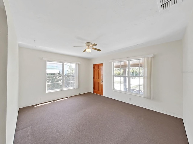 spare room with a ceiling fan, visible vents, and dark carpet