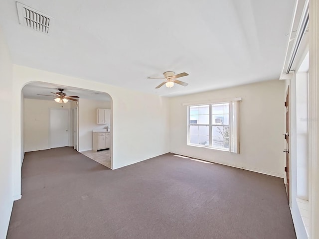 empty room featuring carpet, arched walkways, visible vents, and ceiling fan