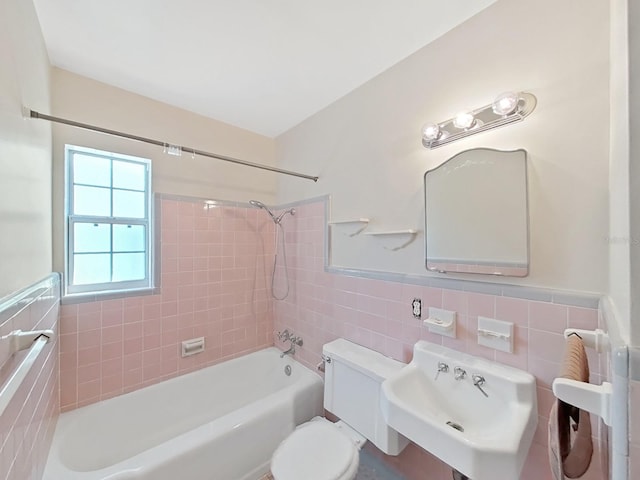 bathroom with a wainscoted wall, toilet, a sink, tile walls, and bathtub / shower combination