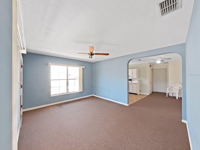 unfurnished room with visible vents, arched walkways, carpet, baseboards, and ceiling fan