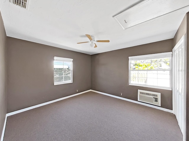 carpeted empty room with a wall mounted air conditioner, visible vents, baseboards, and ceiling fan