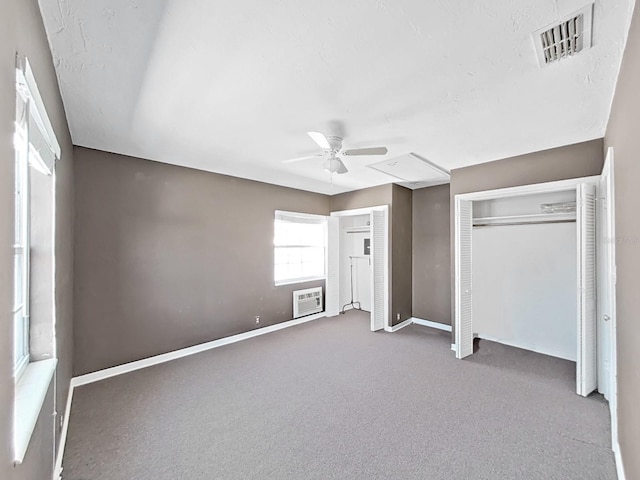 unfurnished bedroom with a wall unit AC, carpet, visible vents, baseboards, and ceiling fan