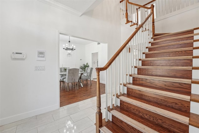 stairway featuring crown molding, tile patterned flooring, a chandelier, baseboards, and a towering ceiling