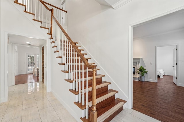 stairway with wood finished floors, a towering ceiling, and crown molding