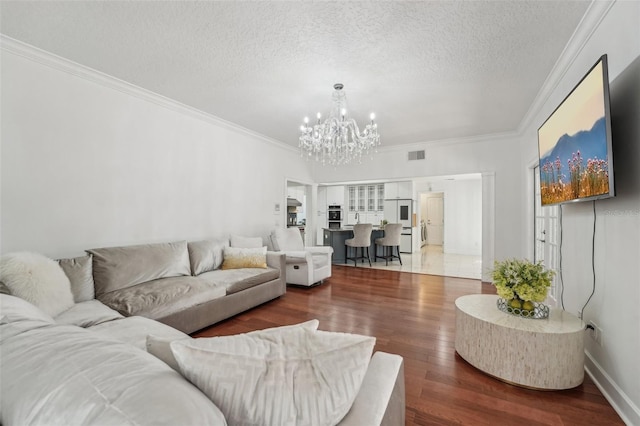 living area with visible vents, a chandelier, ornamental molding, wood finished floors, and a textured ceiling