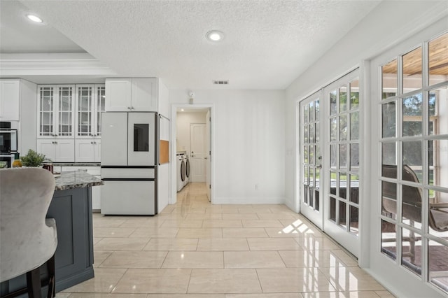 kitchen featuring visible vents, washer and dryer, white cabinetry, freestanding refrigerator, and stone counters