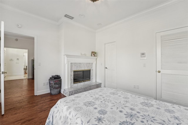 bedroom with a high end fireplace, dark wood finished floors, crown molding, and baseboards