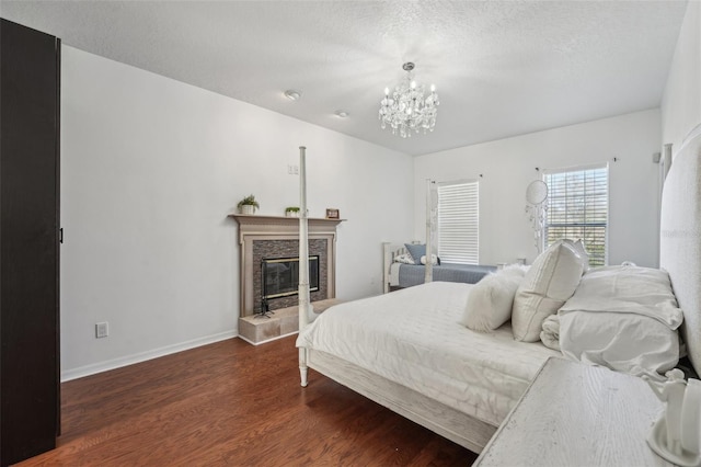 bedroom featuring baseboards, a chandelier, a tile fireplace, wood finished floors, and a textured ceiling