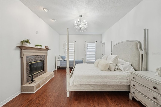 bedroom with baseboards, a fireplace, an inviting chandelier, a textured ceiling, and dark wood-style flooring