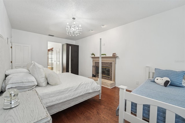 bedroom with visible vents, an inviting chandelier, wood finished floors, a glass covered fireplace, and a textured ceiling