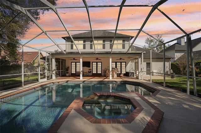 pool at dusk with a ceiling fan, a pool with connected hot tub, french doors, a lanai, and a patio area