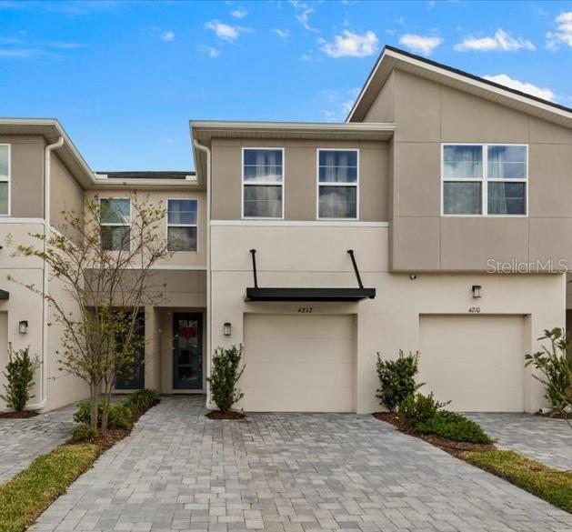 view of property featuring decorative driveway, an attached garage, and stucco siding