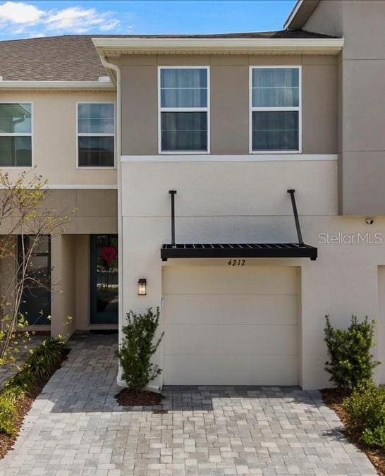 view of property featuring decorative driveway, an attached garage, and stucco siding