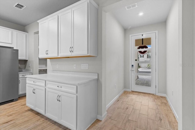 kitchen featuring visible vents, light countertops, freestanding refrigerator, and white cabinetry