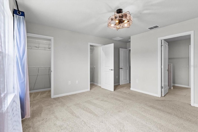 unfurnished bedroom featuring carpet floors, a walk in closet, visible vents, and baseboards