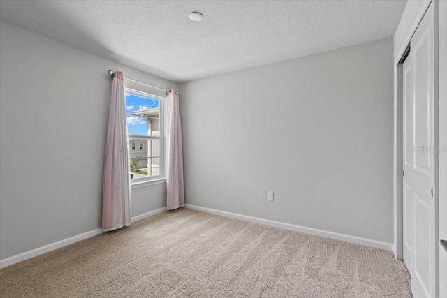 unfurnished bedroom with a closet, light colored carpet, a textured ceiling, and baseboards