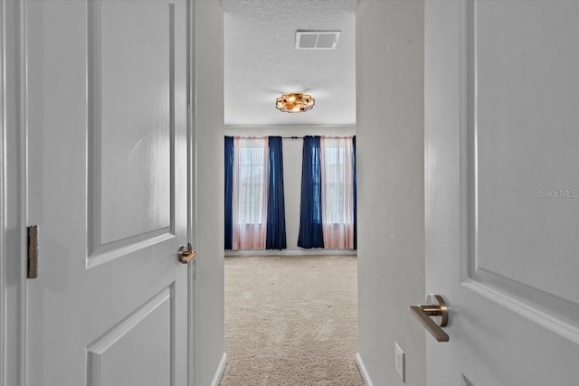 hall with baseboards, a textured ceiling, visible vents, and carpet flooring