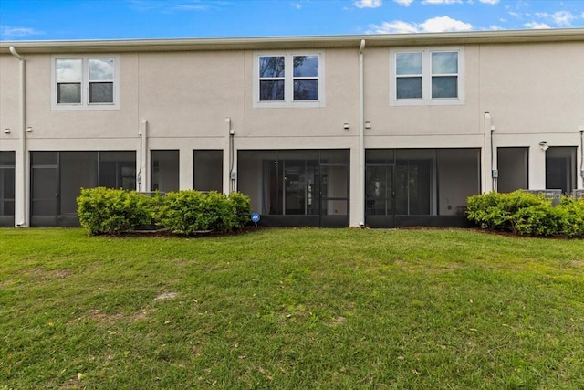 back of property with a lawn, a sunroom, and stucco siding