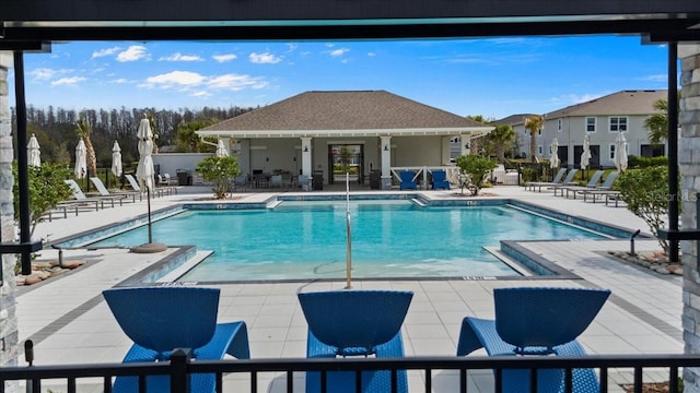 community pool with a patio area, fence, and an outdoor structure