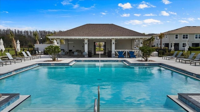 community pool with a patio, an outdoor structure, and fence