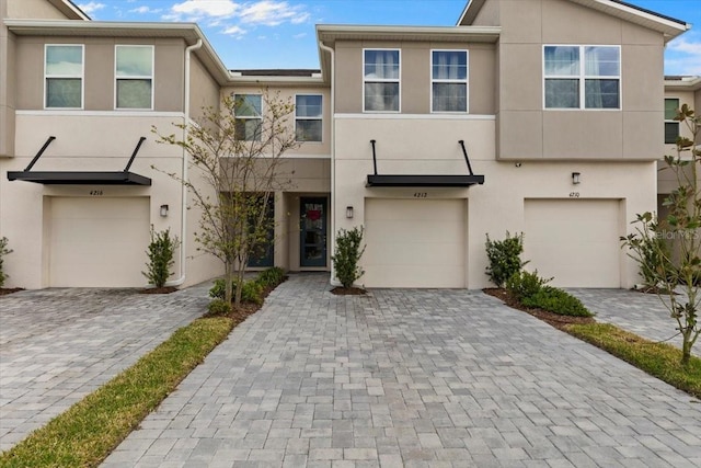 view of property with decorative driveway, an attached garage, and stucco siding