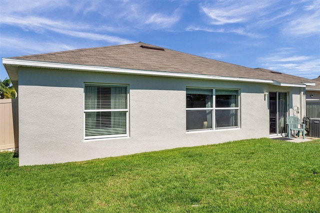 back of property with roof with shingles, a lawn, fence, and stucco siding