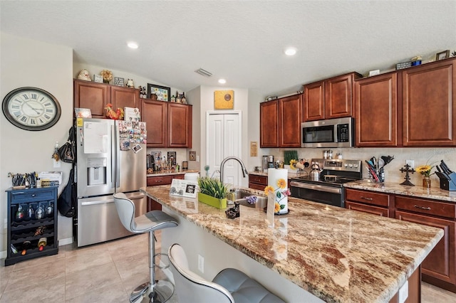 kitchen featuring appliances with stainless steel finishes, a center island with sink, a breakfast bar, and light stone countertops