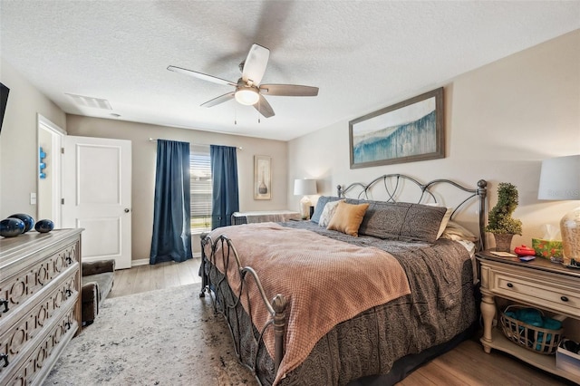 bedroom with a ceiling fan, visible vents, a textured ceiling, and wood finished floors