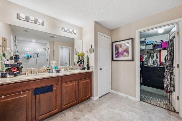 bathroom with a textured ceiling, double vanity, a stall shower, and a sink