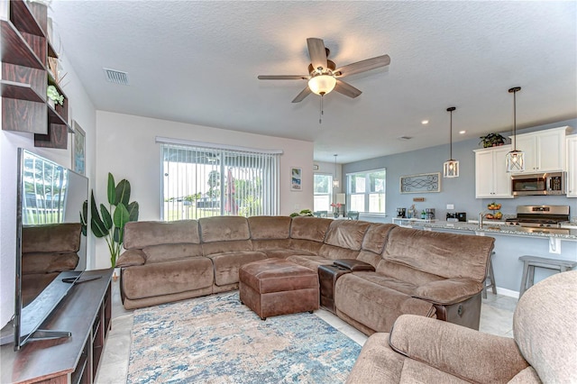 living room with a ceiling fan, visible vents, a textured ceiling, and light tile patterned floors