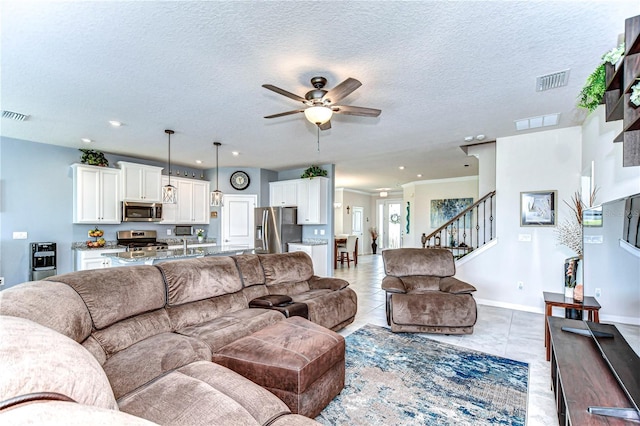 living room with stairs, light tile patterned floors, visible vents, and a ceiling fan