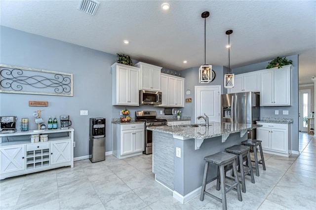 kitchen with stainless steel appliances, a breakfast bar, a sink, visible vents, and white cabinetry