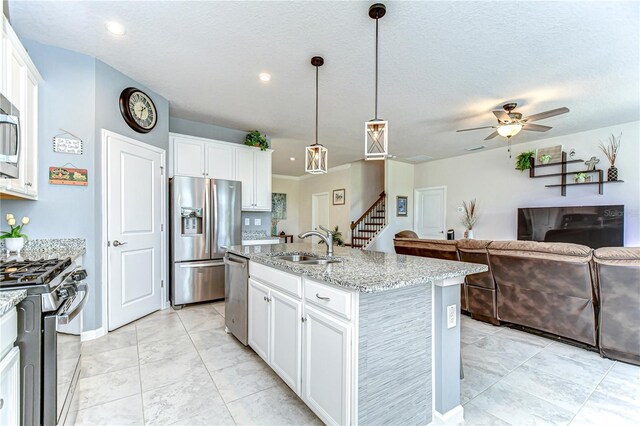 kitchen featuring stainless steel appliances, white cabinets, a center island with sink, and light stone countertops