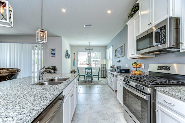 kitchen with appliances with stainless steel finishes, white cabinetry, a sink, and light stone countertops