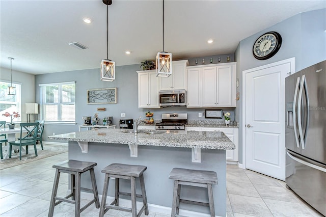 kitchen with appliances with stainless steel finishes, white cabinets, a sink, and a kitchen breakfast bar