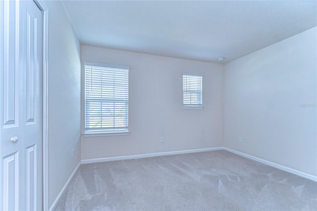 spare room featuring light carpet, plenty of natural light, and baseboards