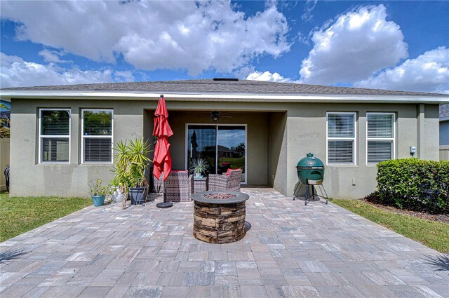 back of property featuring a shingled roof, a fire pit, a ceiling fan, a patio, and stucco siding