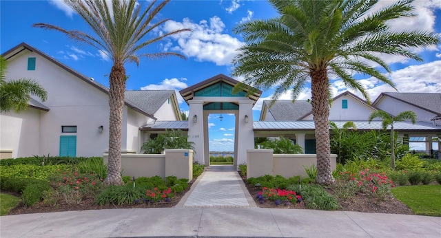 view of front facade featuring metal roof, a fenced front yard, a gate, stucco siding, and a standing seam roof