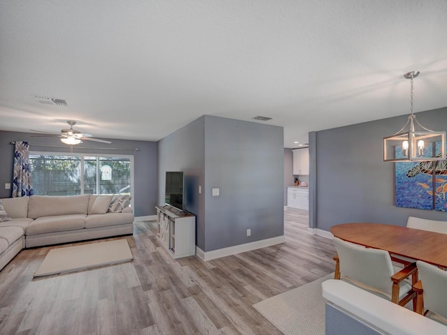 living room featuring light wood-style floors, baseboards, visible vents, and ceiling fan with notable chandelier