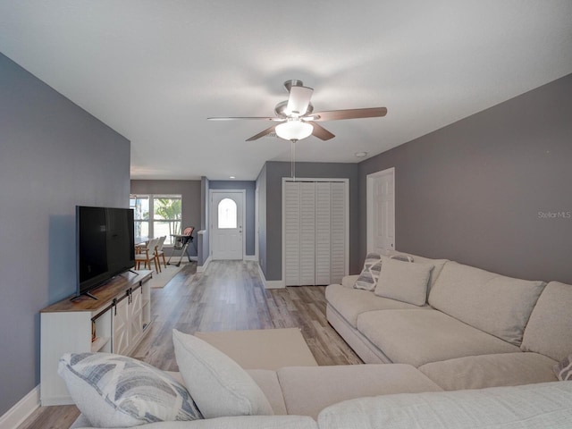 living area with light wood-style floors, ceiling fan, and baseboards