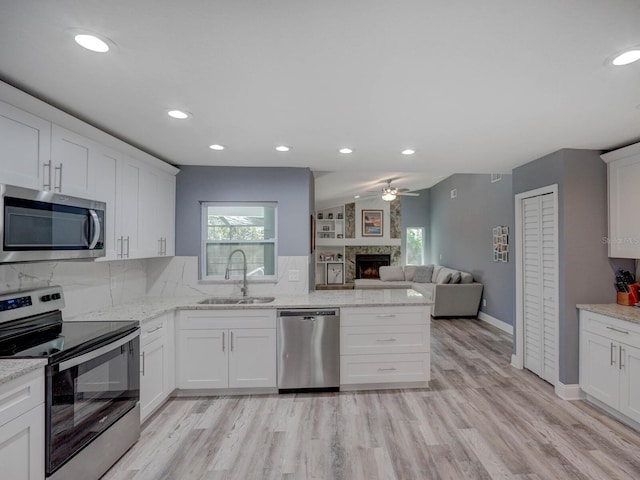 kitchen featuring a large fireplace, appliances with stainless steel finishes, a sink, and a wealth of natural light